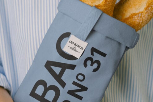 Close up of blue fabric bag mockup showing Les Basics label with baguettes in background