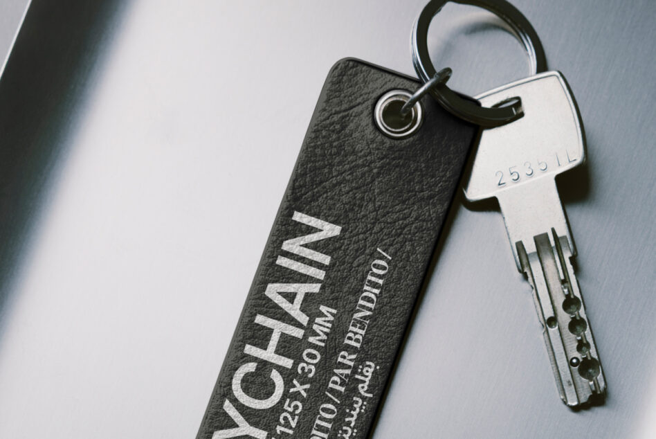 Dark charcoal leather keychain with white stamped text alongside silver key