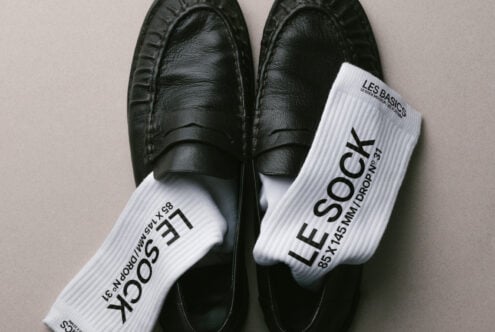 Black loafers displayed with white ribbed socks on neutral background