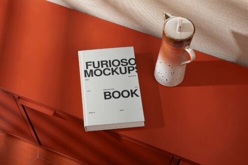 White hardcover book on burnt orange surface next to terracotta ceramic vessel