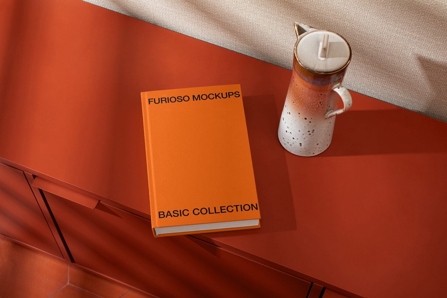 Orange hardcover book with ceramic candle on red surface