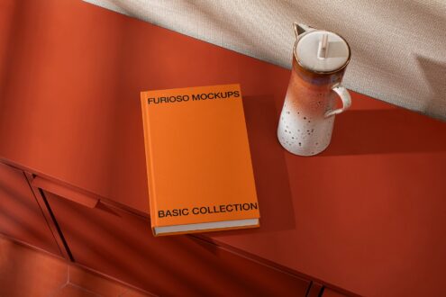 Orange hardcover book with ceramic candle on red surface
