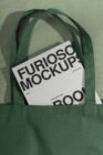 Green canvas tote bag holding branded mockup documents inside