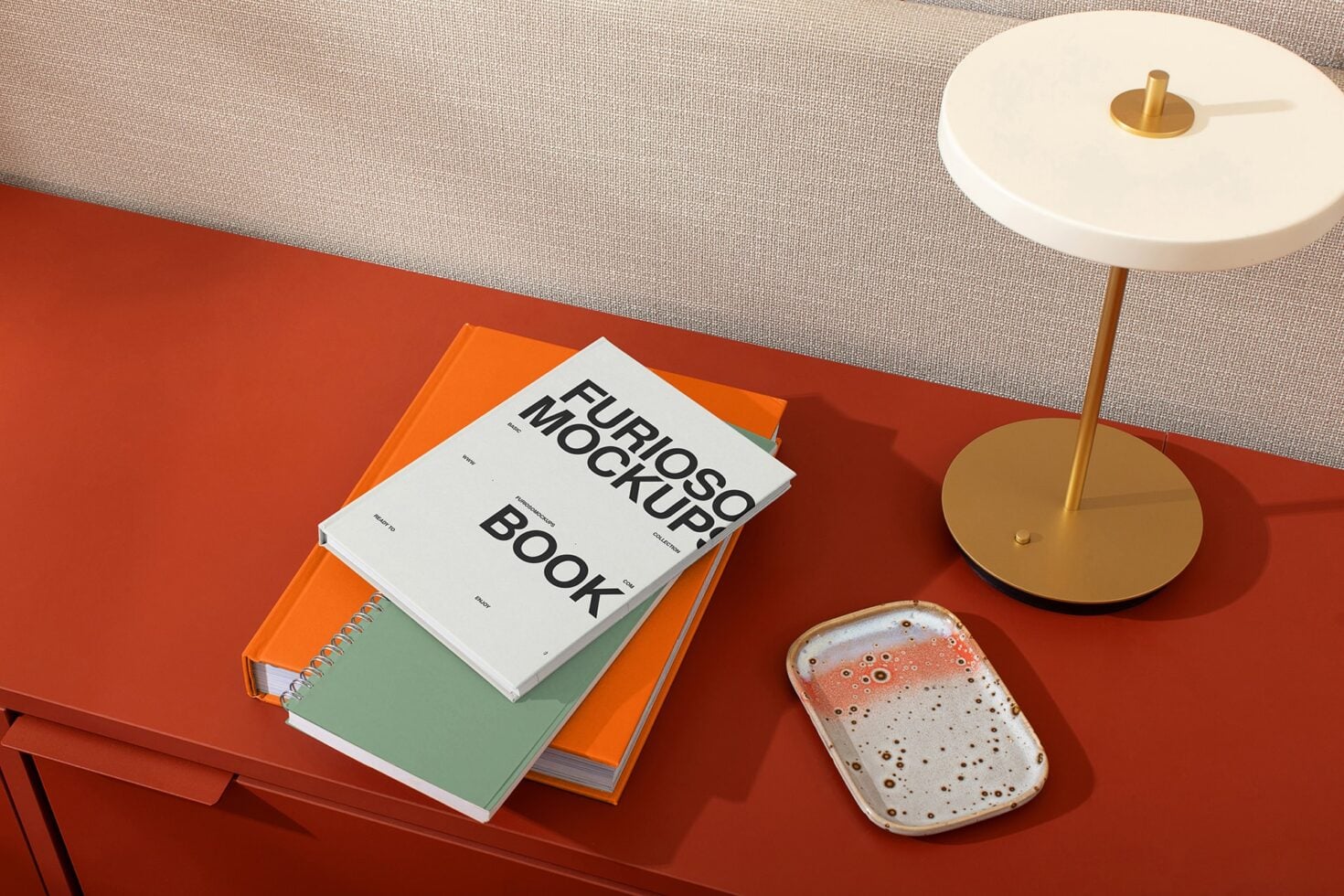 Three colorful spiral bound books stacked on red surface near gold lamp with white shade