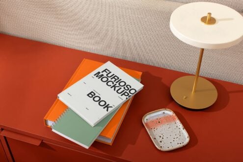 Three colorful spiral bound books stacked on red surface near gold lamp with white shade