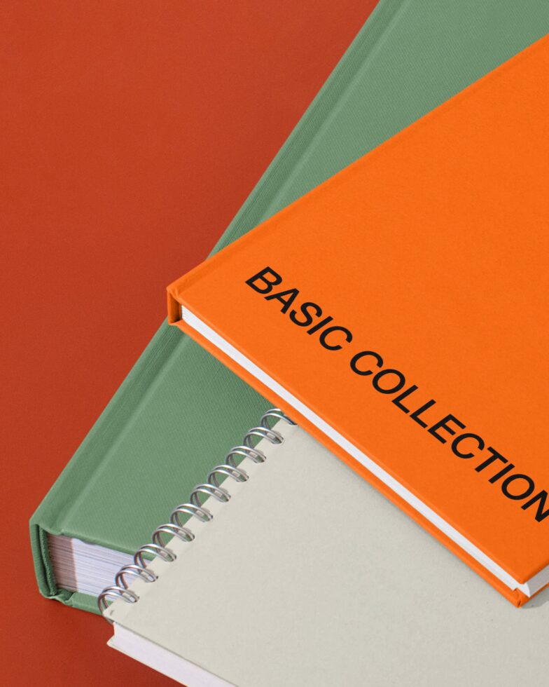 Stacked spiral notebooks in orange with Basic Collection label on red table with lamp
