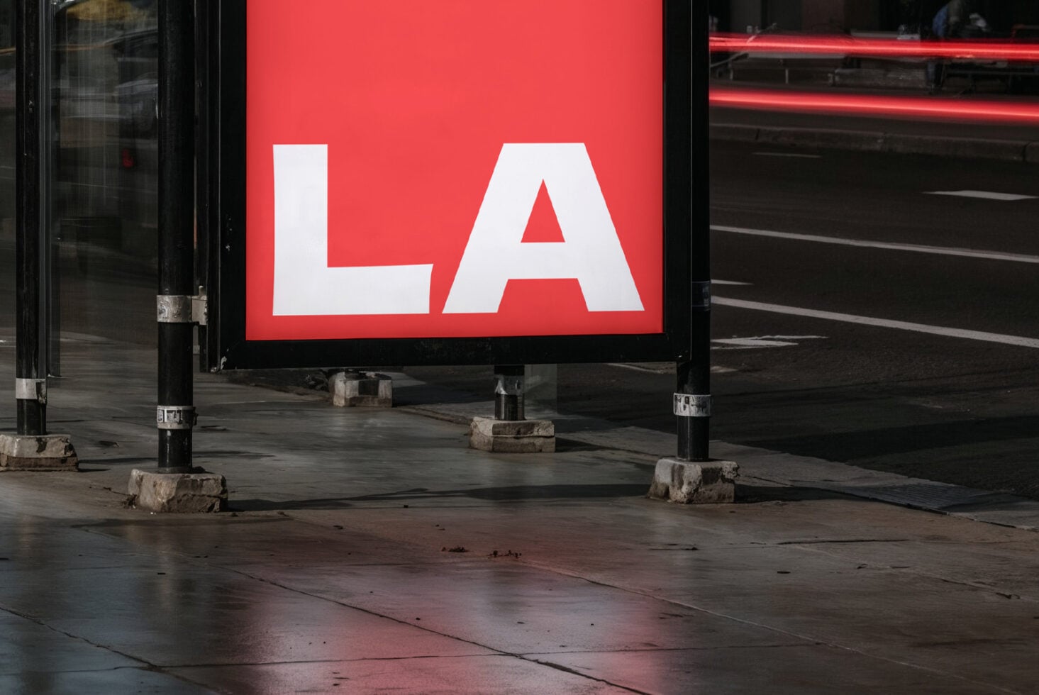 Red billboard with white LA letters mounted on wet urban street at dusk