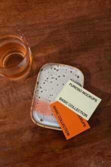 Stacked white business cards next to amber glass on wooden table flat lay