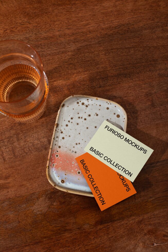 Stacked white business cards next to amber glass on wooden table flat lay