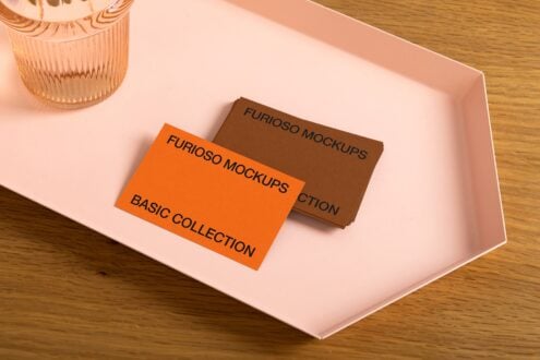 Brown cardstock with orange business card on pink surface next to glass vase