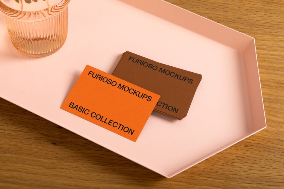 Brown cardstock with orange business card on pink surface next to glass vase