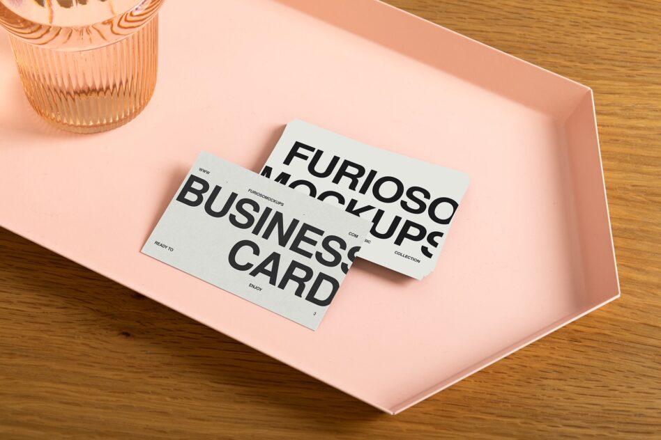 Two white business cards on pink hexagonal tray with peach glass