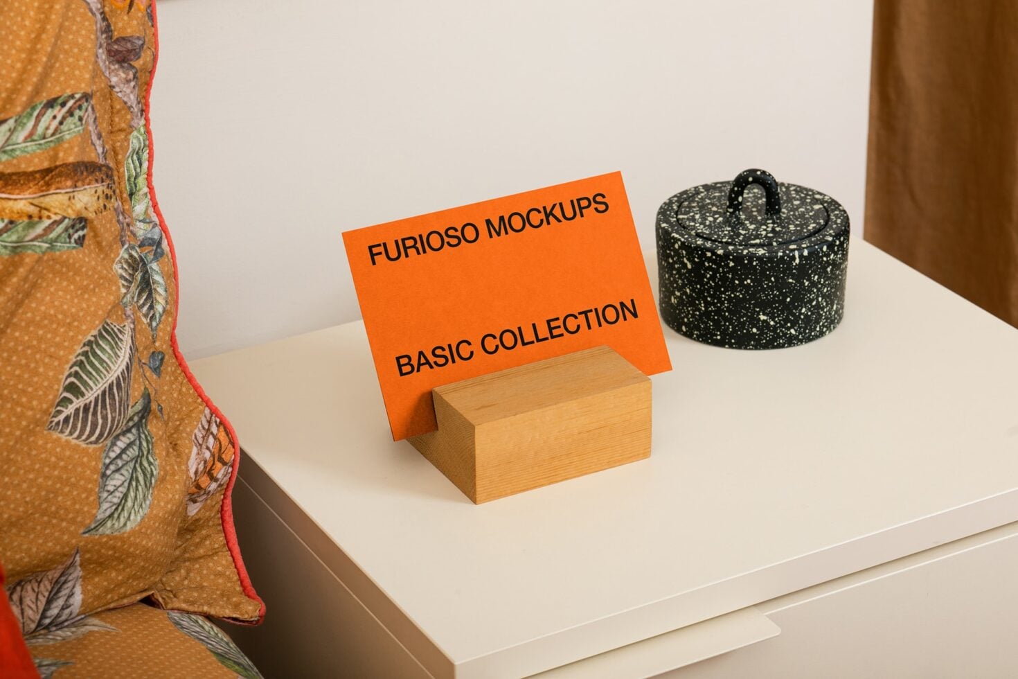 Orange banner on wooden box surrounded by patterned fabric, ceramic pot