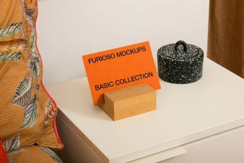 Orange banner on wooden box surrounded by patterned fabric, ceramic pot