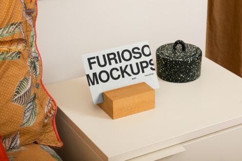 White card mockup on wooden block with patterned fabric, dark pot nearby