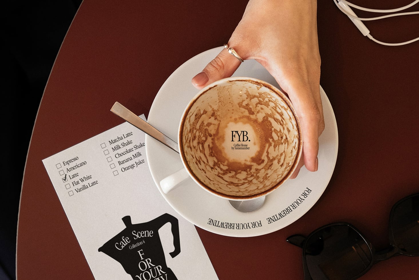 Overhead shot of latte with latte art, coffee order checklist, sunglasses on burgundy table