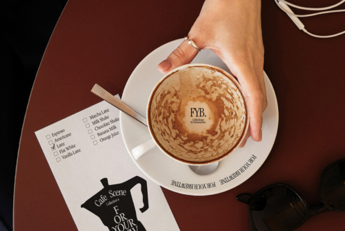 Overhead shot of latte with latte art, coffee order checklist, sunglasses on burgundy table