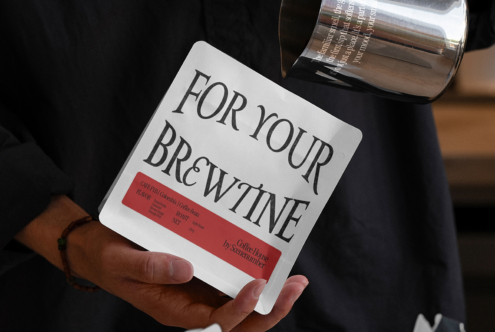 White coffee bag mockup with red accent label being held in flat lay setup