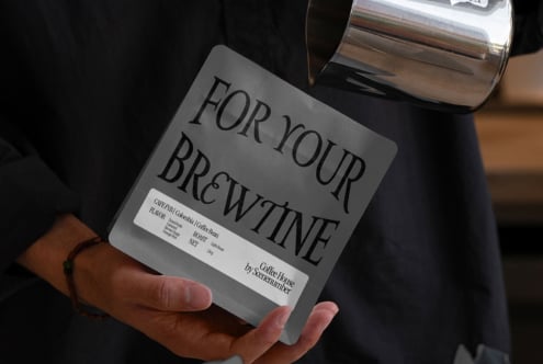 Gray coffee bag mockup held in hand with white label on dark background
