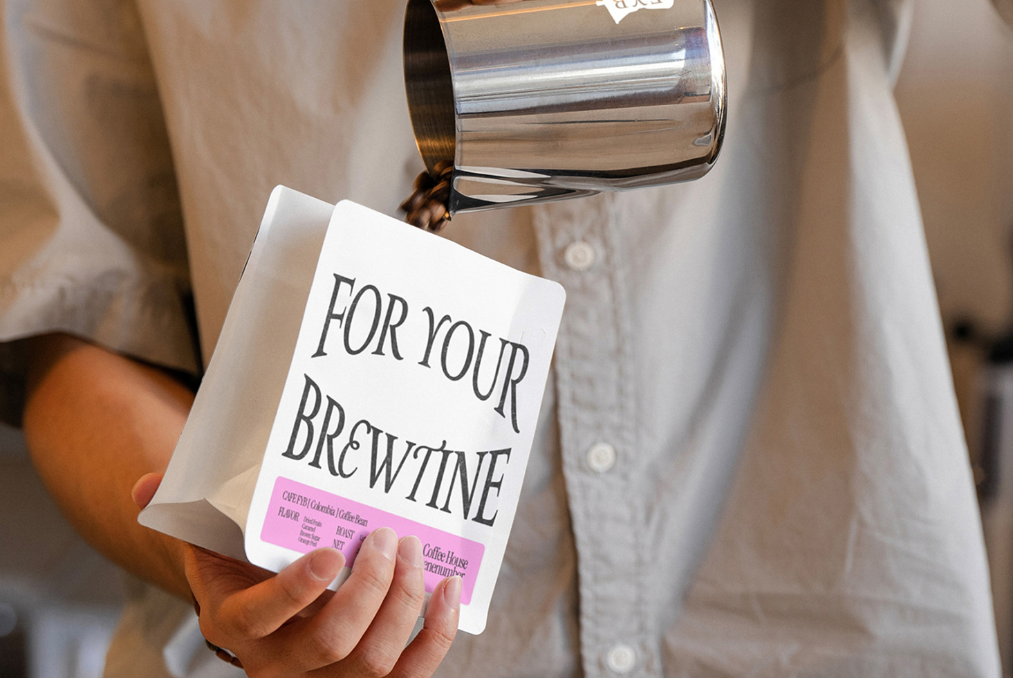 Woman in light shirt holding white coffee bag with bright pink label detail, pitcher tilted