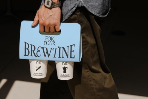 Hand carrying light blue coffee cup holder with two branded cups attached