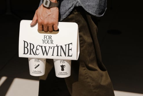 Person carrying light-colored coffee cup holder with two branded cups inside