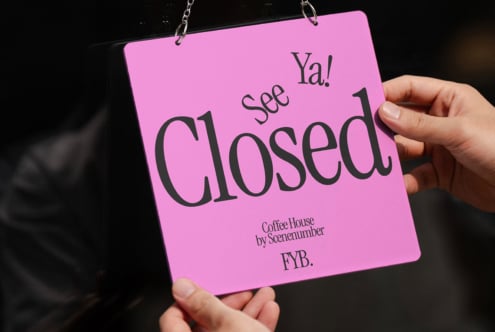 Hand holding bright pink Closed see ya door sign against black background on chain