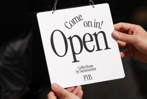 Hands holding Come on in Open door sign against dark background with chain hanger