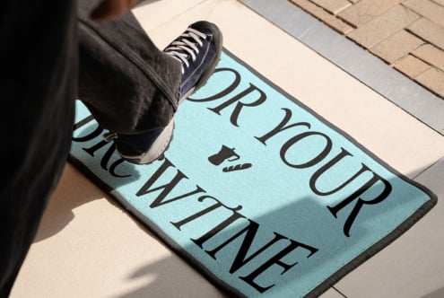Bright blue doormat mockup with large serif text, foot stepping on entryway
