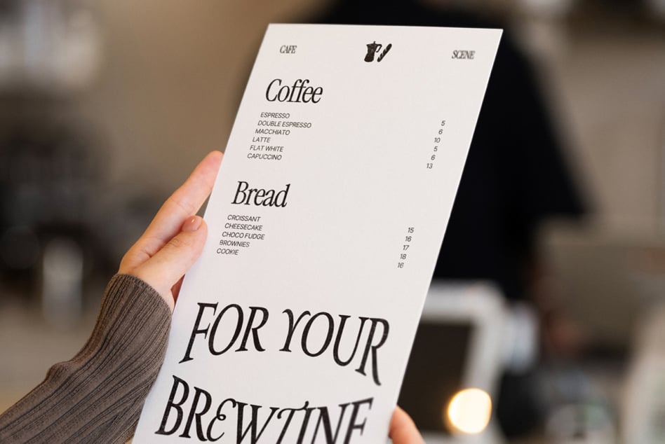 Hand holding printed cafe menu with coffee, bread, pricing listed