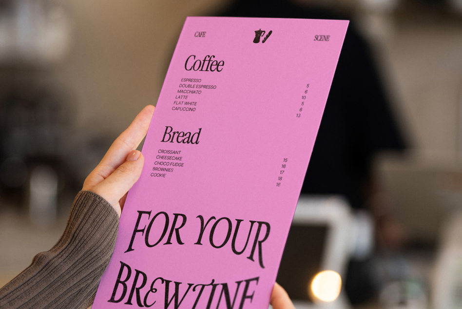 Hand holding bright pink menu with coffee, bread items, browline typography