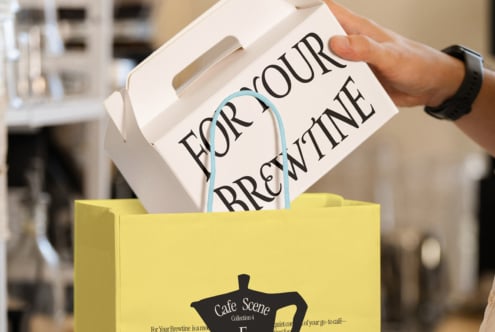 Yellow shopping bag holding white coffee cup with blue handle, cafe scene mockup