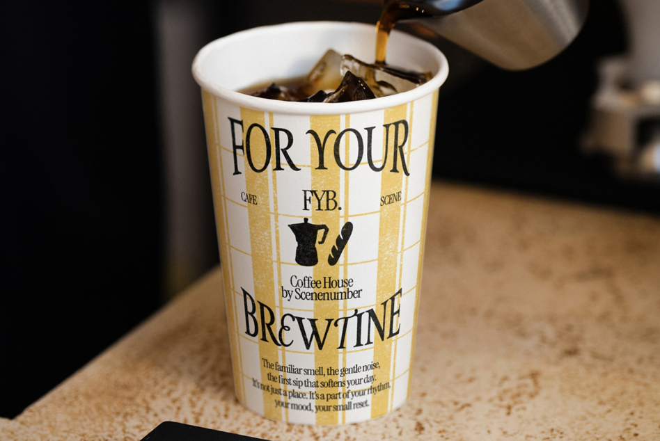 Gold striped paper cup with black serif text pouring espresso into white interior