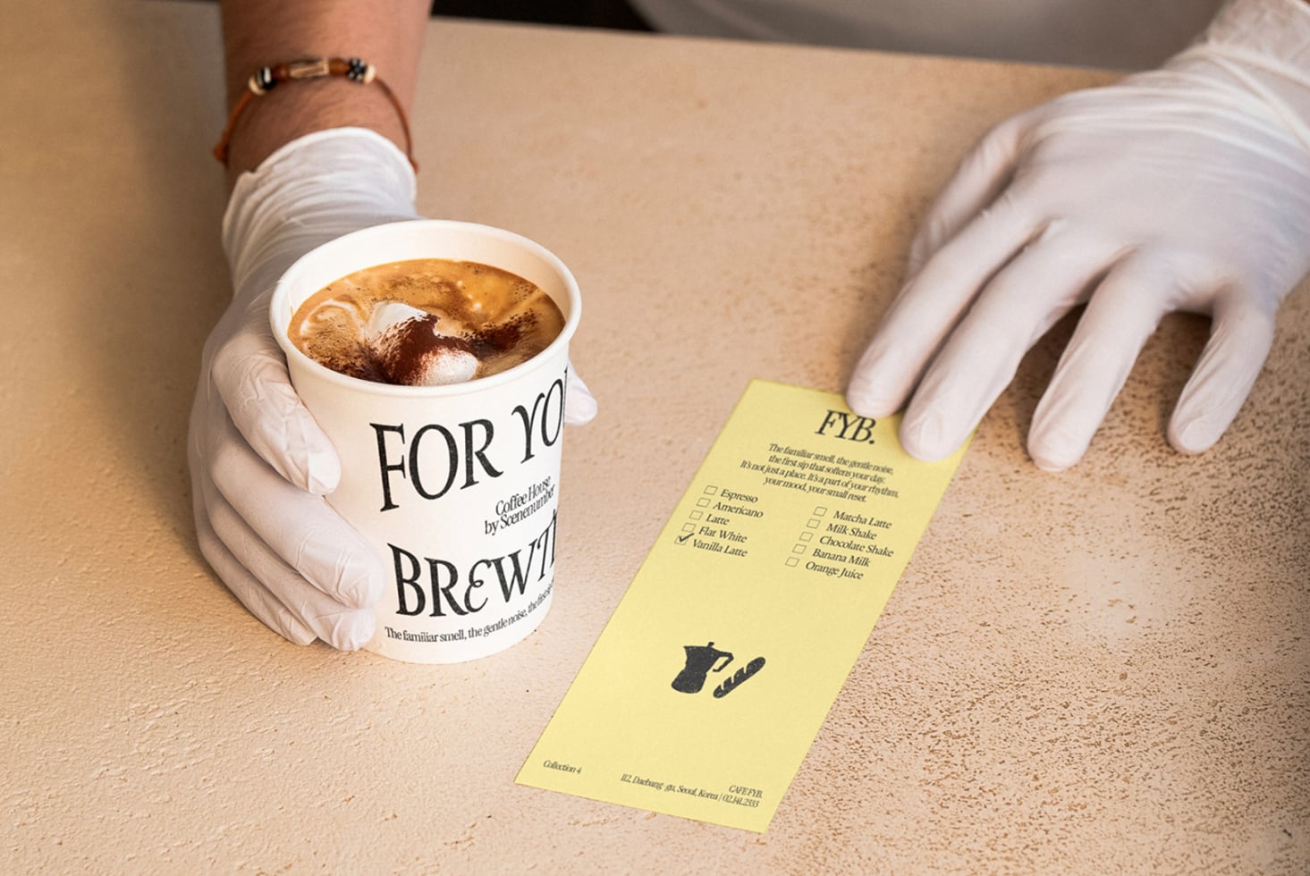 White gloved hands holding yellow menu card next to cup with latte art on beige surface