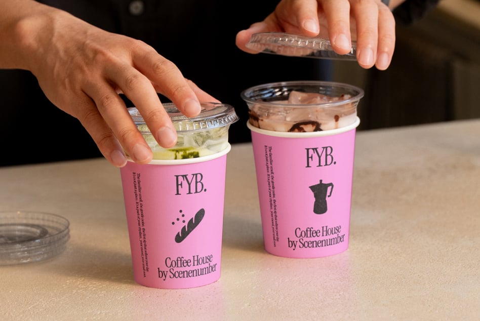 Two pink paper cups being held with clear lids, iced beverages inside