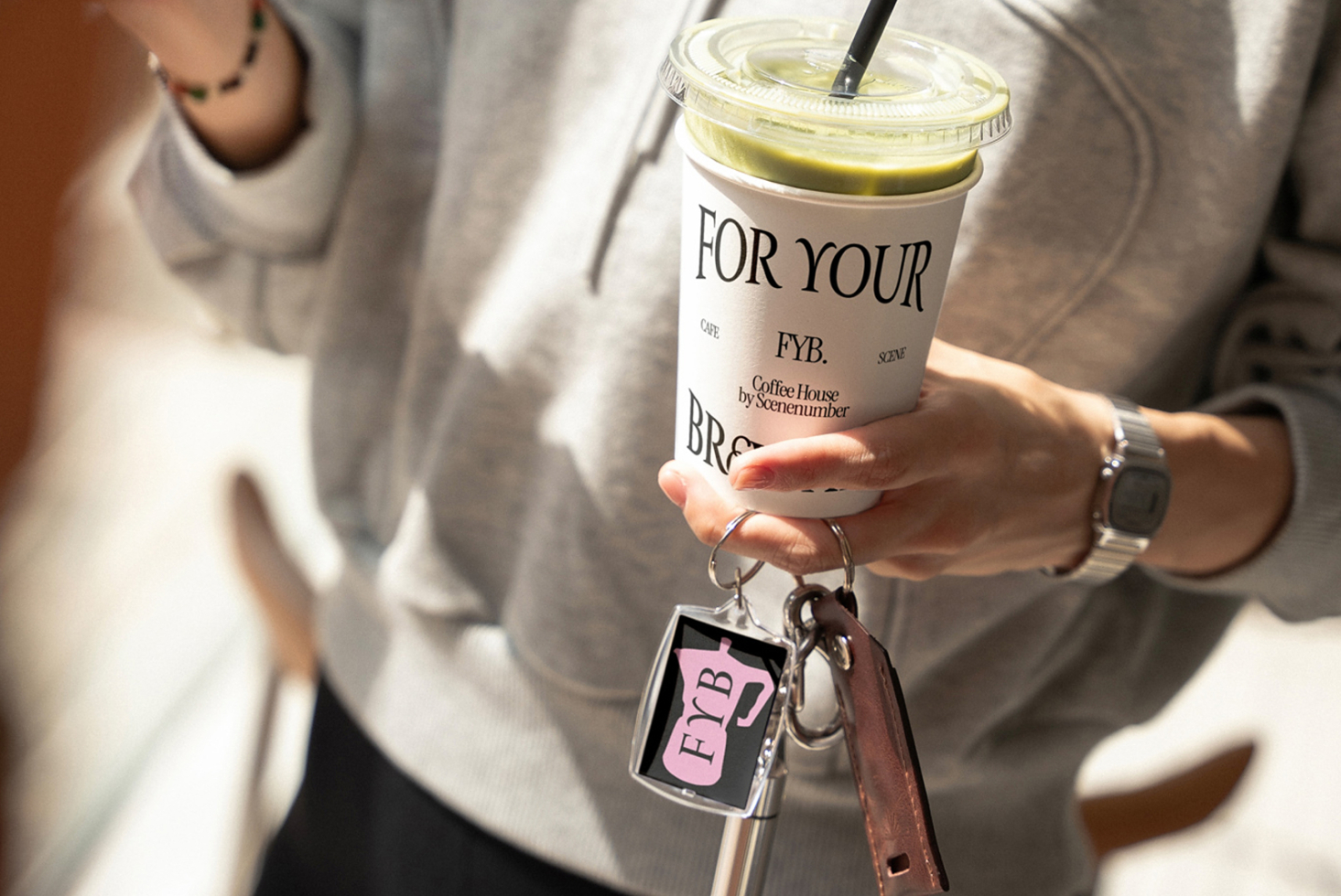 Woman holding iced matcha drink with FYB keychain, wearing cream sweater