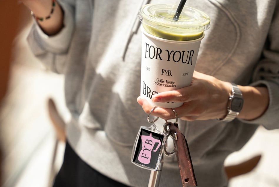 Woman holding iced matcha drink with FYB keychain, wearing cream sweater