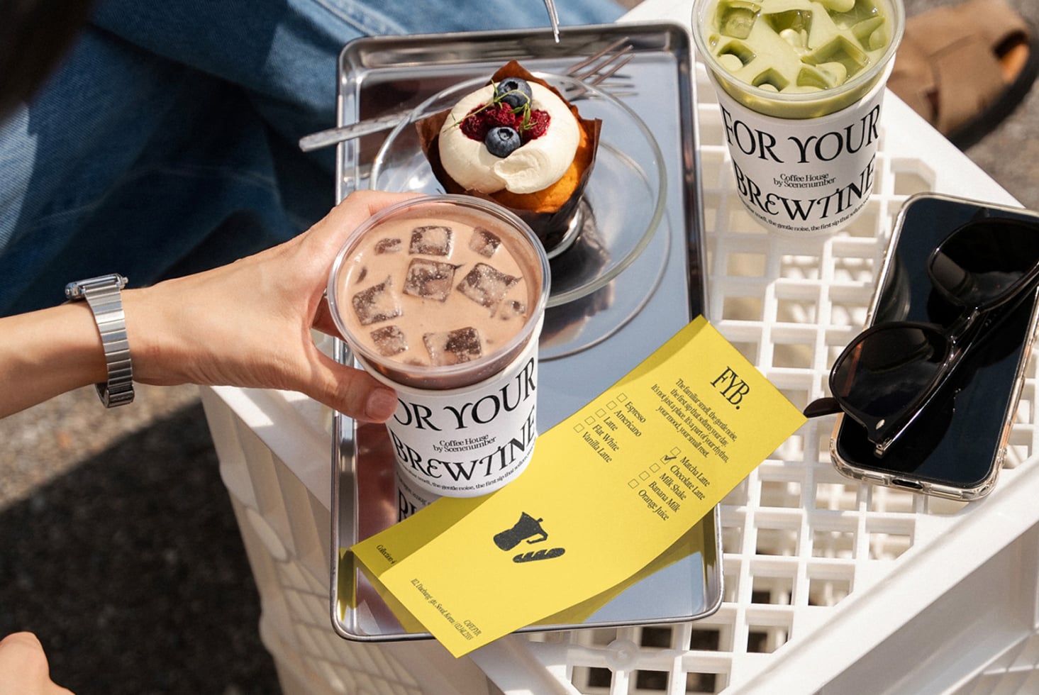 Overhead shot of iced coffee cup, pastry with berries, yellow FYB menu card
