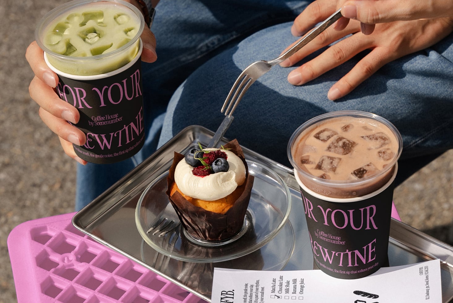 Branded paper cups with dessert on tray, pink plastic crate, notepad, sunlight scene