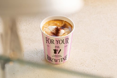 Pink branded coffee cup with latte art, sitting on neutral surface with soft lighting