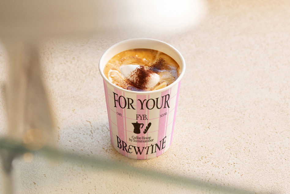 Pink branded coffee cup with latte art, sitting on neutral surface with soft lighting