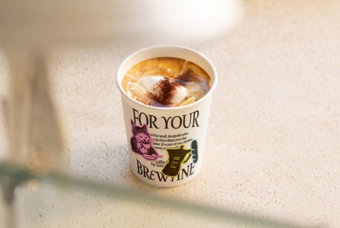 Coffee cup with latte art topped with cocoa powder, branded cup sleeve showing cafe name