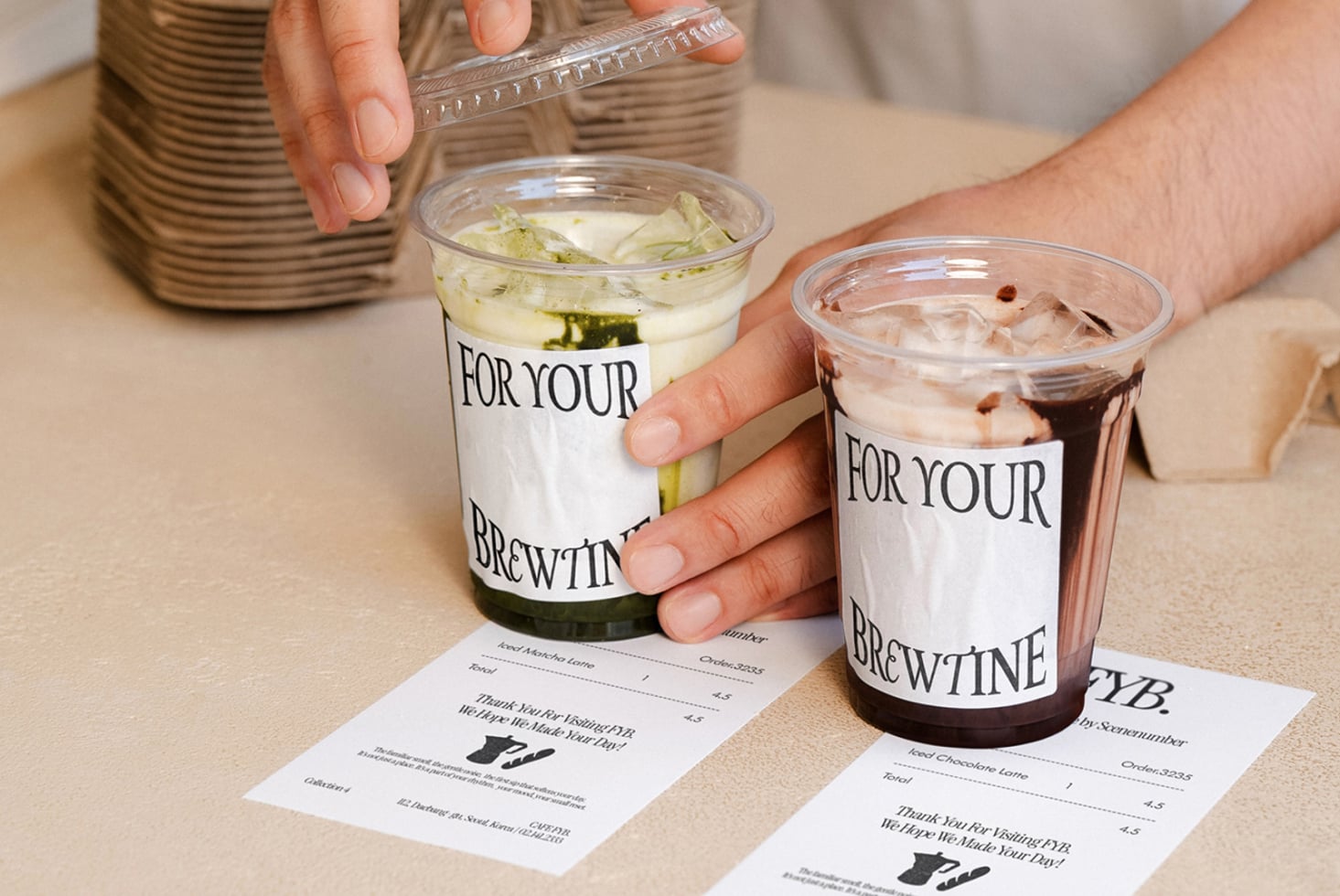 Hands holding two iced drinks with branded cups, receipts on table below