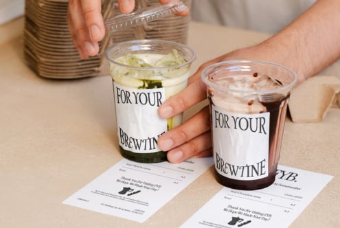 Hands holding two iced drinks with branded cups, receipts on table below