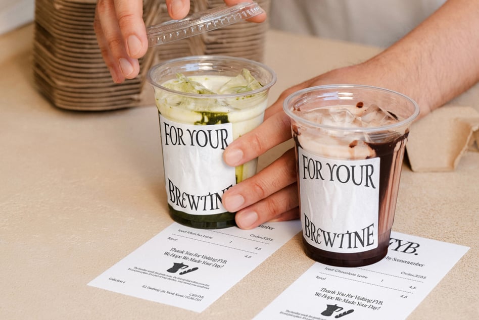 Hands holding two iced drinks with branded cups, receipts on table below