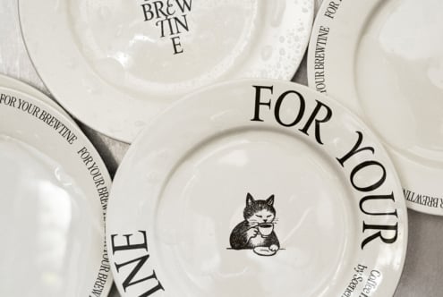 Cream colored stacked plates with cat holding cup, For Your Brewtine text on rim