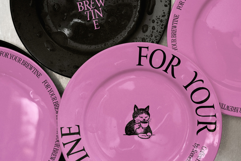 Overhead shot of pink ceramic plates stacked with cat illustration, For Your Brewtine text