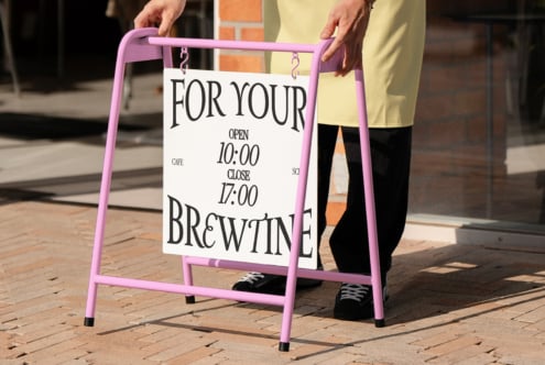 Pink sandwich board sign with cafe hours mockup held by person outdoors