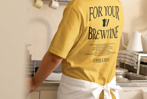 Yellow tee with brewpub text design mockup shown on person in kitchen setting