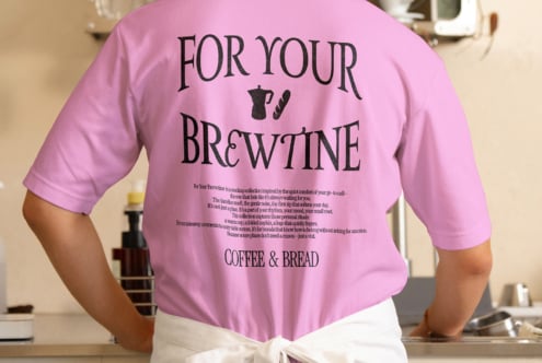 Pink tee with coffee branding on back, styled with cream apron in kitchen